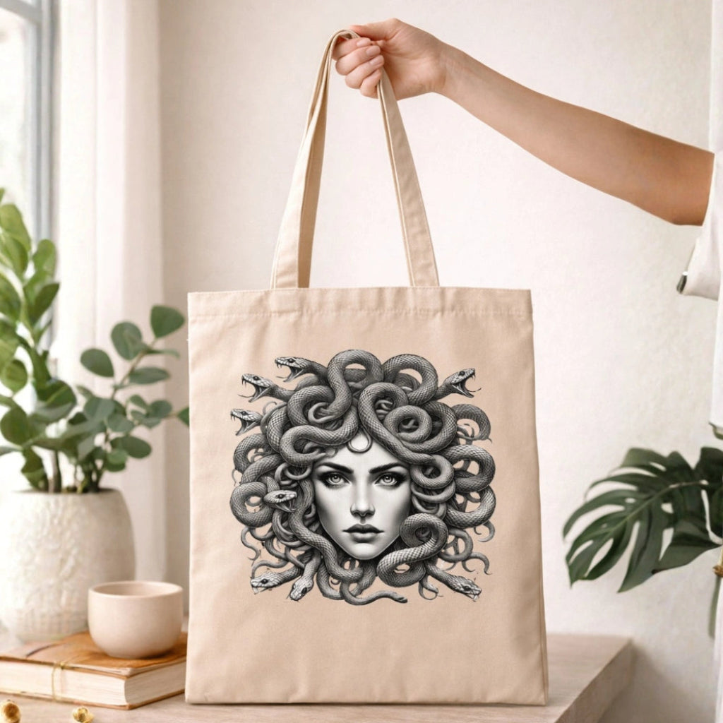 Beige tote bag with detailed Medusa artwork, featuring snake hair, held indoors by a hand