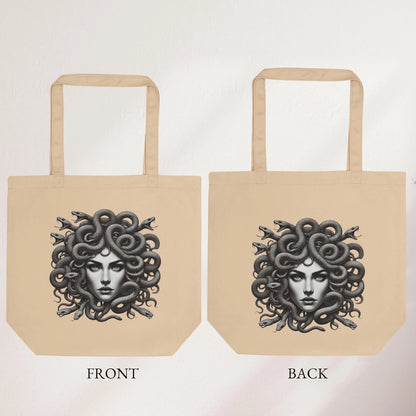 Beige tote bag with detailed Medusa artwork, featuring snake hair, held indoors by a hand