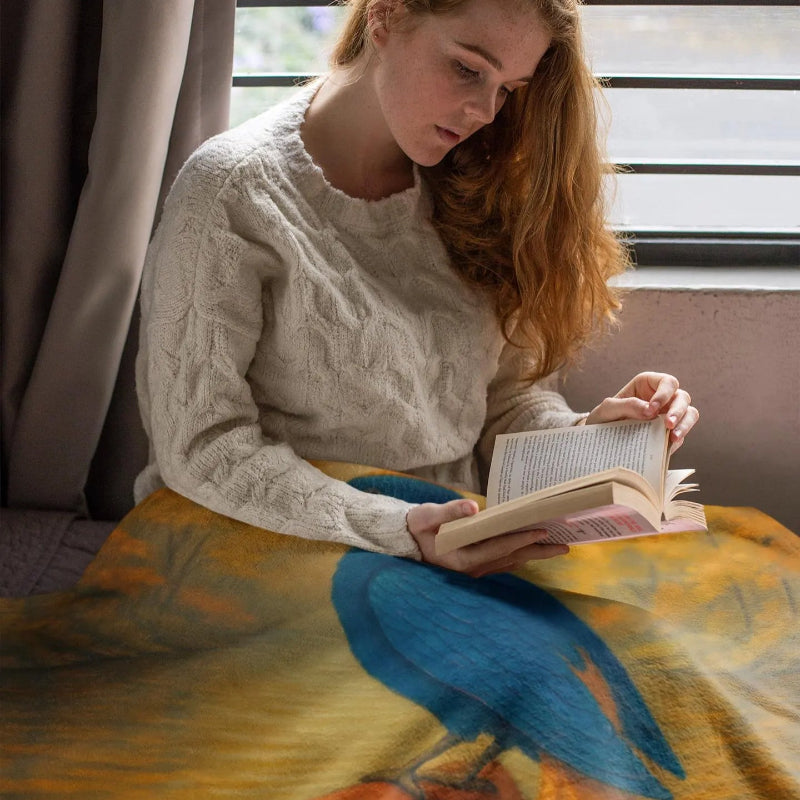 Woman reading with plush blanket featuring a colorful phoenix bird design