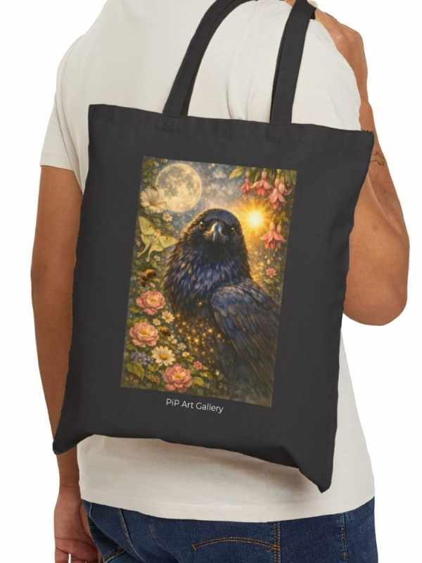 Black tote bag with a mystical raven illustration, moon, flowers, and glowing light